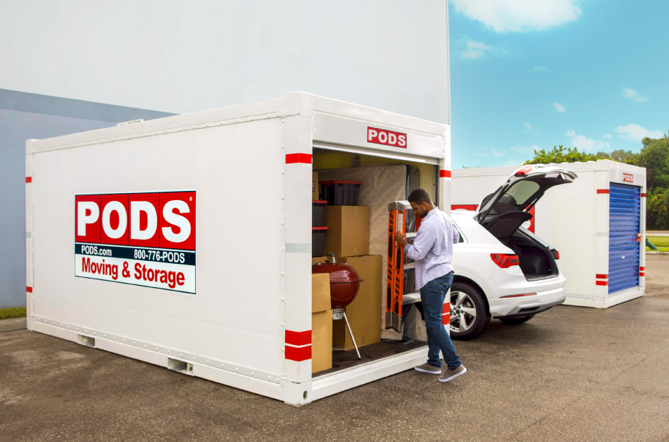 A man is putting a ladder into his loaded PODS portable storage container, which is currently sitting outside a secure PODS Storage Center.