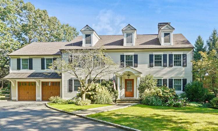 A two-story Colonial home in Rye, New York. The home features a white exterior with blue shutters and a two-door, two-car garage.