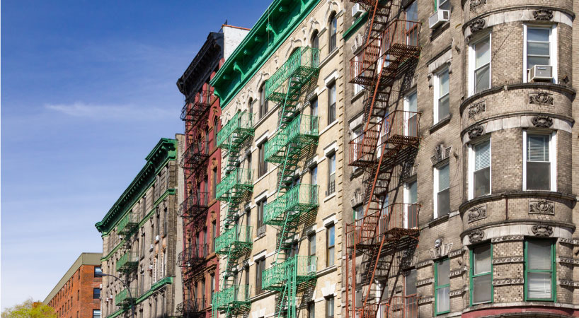 A street-level view, looking up at a row of colorful and historic residential buildings at the intersection of Mott and Kenmare Streets in Manhattan’s NoLita neighborhood, among the safest neighborhoods in New York City.