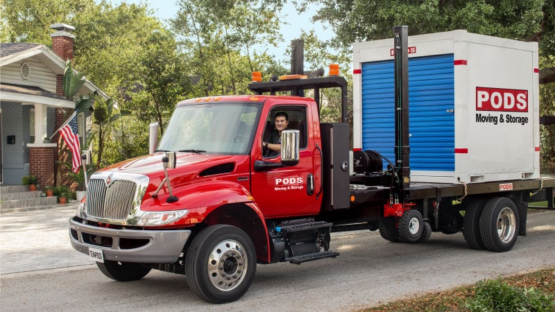 A PODS truck driver transports a PODS portable storage container through a residential neighborhood.