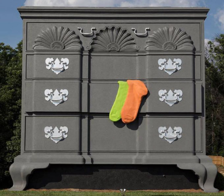 The world's largest chest of drawers in North Carolina. It is a gray chest, with fleur-de-lis handles. A yellow sock and an orange sock hang out of one of the drawers.