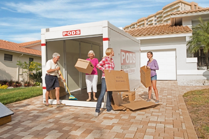 A woman and her teenaged daughter work together to break down moving boxes beside a PODS portable container after helping elderly parents move into a new home.