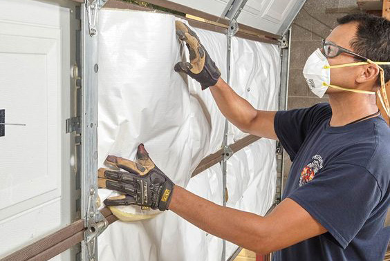 A contractor installs white insultation panels while wearing a white safety mask