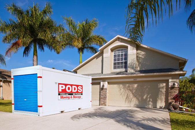  Exterior view of a two-story house in Florida with palm trees in the yard and a PODS portable moving container in the driveway.
