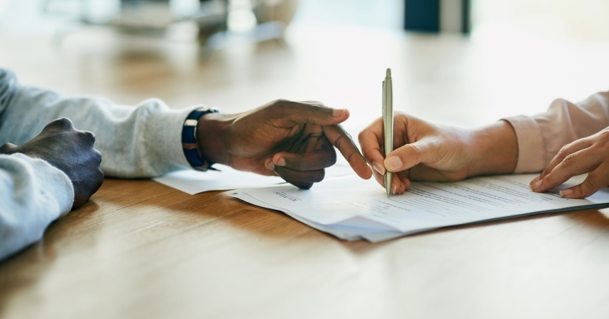 A car shipping representative pointing out a clause in a contract to a customer as they prepare to sign it.
