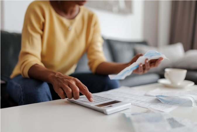 A woman is looking at a receipt and using a calculator to add up her expenses