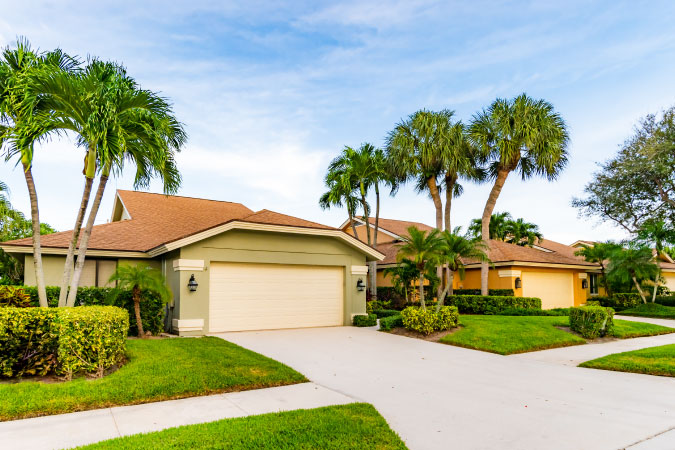 Three single-story residential homes in Florida with neatly trimmed hedges, decorative palms, and green lawns.