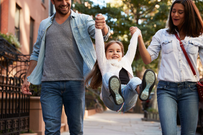 A mom and dad swinging their daughter in their arms while walking in a new city
