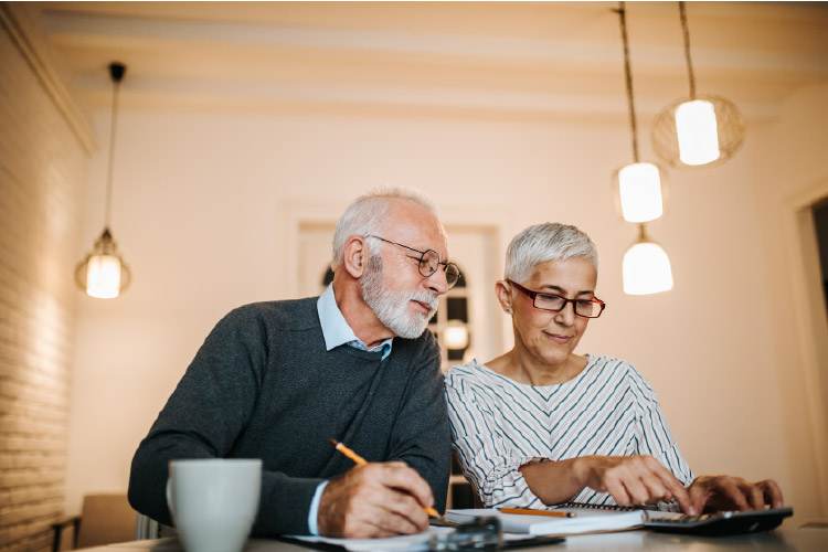 A couple is using a calculator and taking notes on paper, trying to figure out how much they need to save for retirement. 