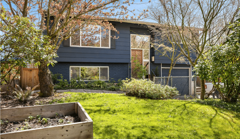 A boxy, two-story home in the St. Johns neighborhood of Portland, Oregon, featuring a combination brick and siding exterior and painted a dark blue. 