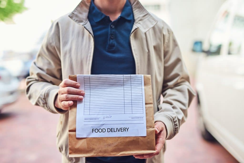 Man delivering a restaurant takeout order via curbside pickup to a doorstep