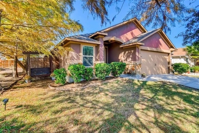 A pink and cream-colored residential home in Pflugerville, Texas. Trees in the yard cast shadows on the house and lawn.