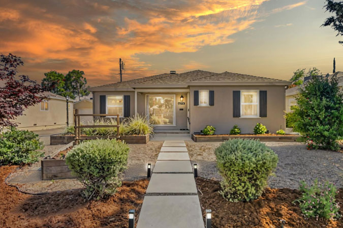 Exterior sunset view of a one-story home in Tahoe Park — one of the best neighborhoods in Sacramento — featuring a stucco exterior, entry pavers, and an expertly landscaped yard.