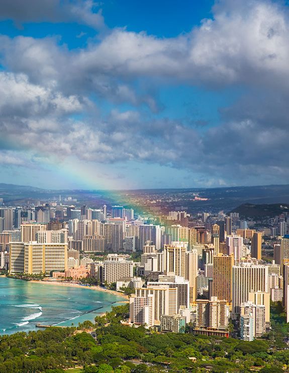 An aerial shot of the city of Honolulu. A rainbow hangs overhead the city.