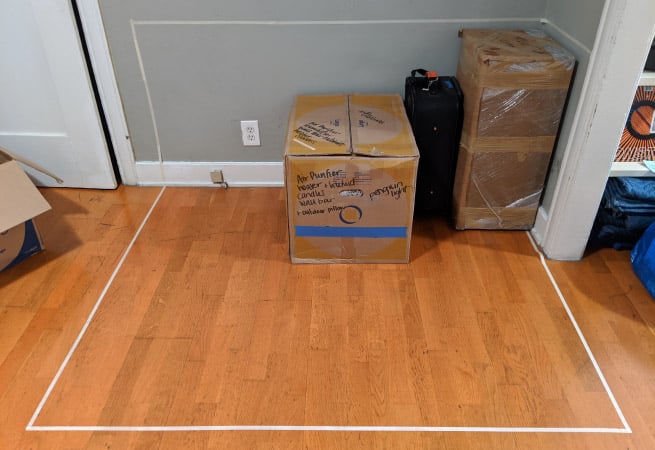 A few boxes have been arranged in the taped-off corner of a room, which is meant to represent the available space in a moving container.