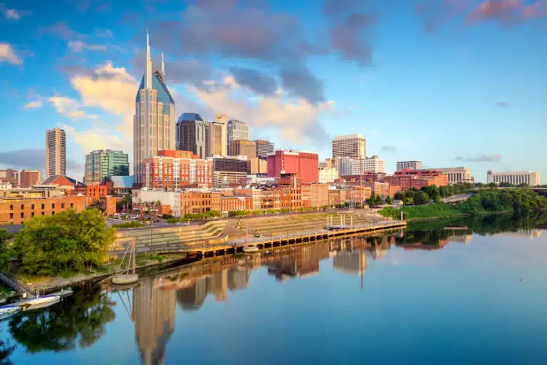 View of Downtown Nashville seen from across the Cumberland River just after sunrise, featuring a distinct city skyline and a placid waterfront.