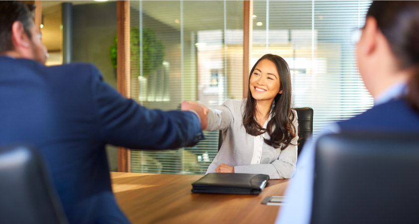A woman gladly accepts a new job, shaking hands with her interviewers