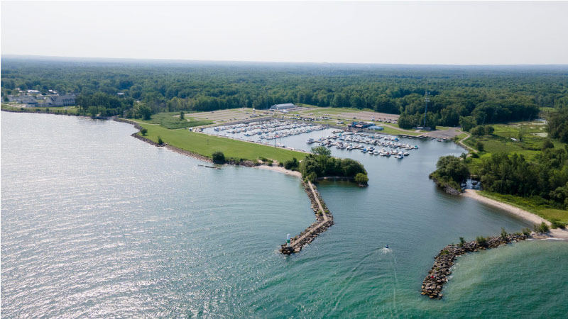 Aerial view of the Geneva Marina in Geneva-on-the-Lake, OH, on a sunny day. The light is reflecting off the water and the surrounding area is lush with trees.