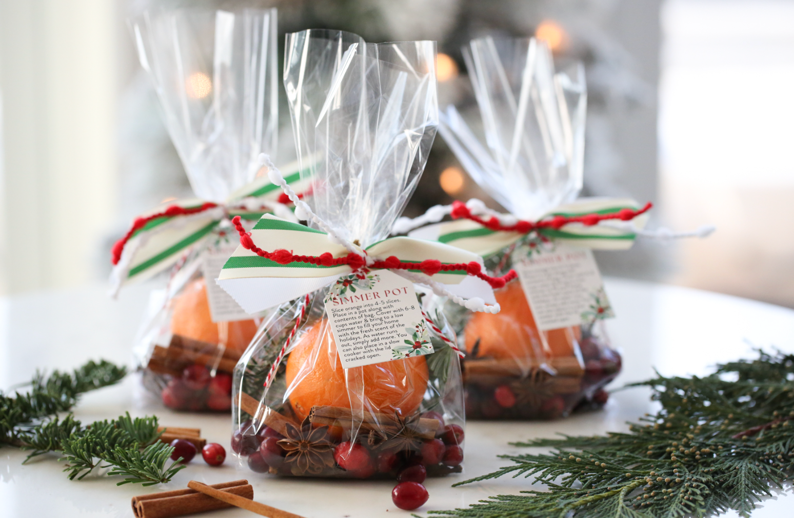Three simmer potpourri bags sit on a table surrounded by greenery, making for aromatic last-minute DIY Christmas gifts.