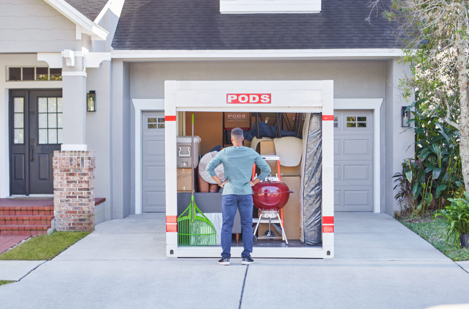 A man is standing in his driveway at the front of his loaded PODS portable storage container — one of the best local moving and storage options for flexibility.