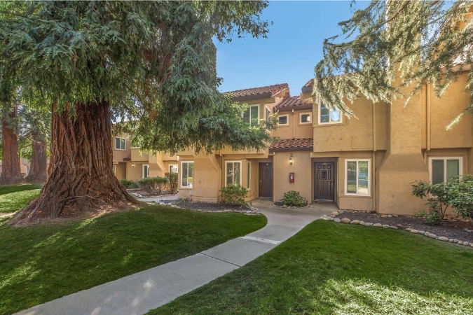 A row of tan townhomes surrounded by green lawns, mature trees, and a curved walkway, highlighting a peaceful residential setting for those moving to Sacramento.