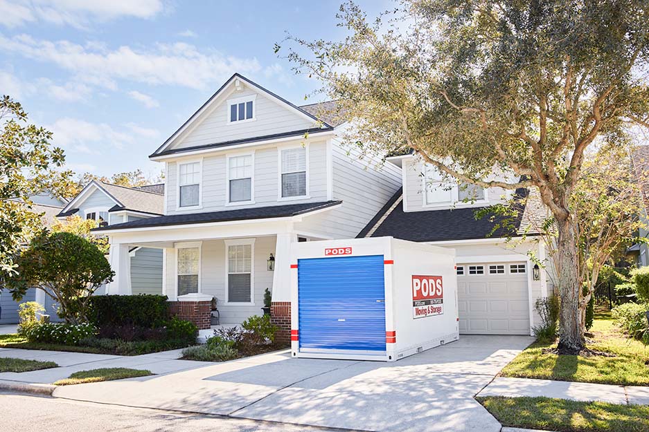 A PODS moving and storage container on a driveway of a white multi-story home.