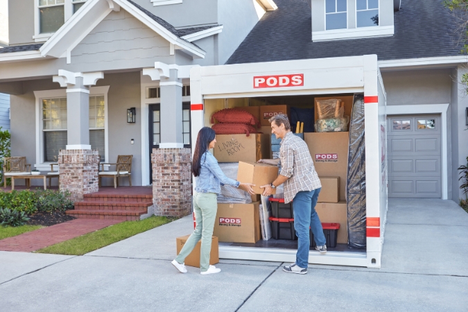 A couple loading a PODS portable storage container in the driveway of their new home while learning how to combine two households before moving in together.