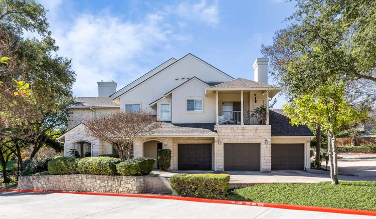 A large, two-story home in Austin’s Allandale neighborhood, featuring three single garage doors, a chimney, and a low stone wall in the front.