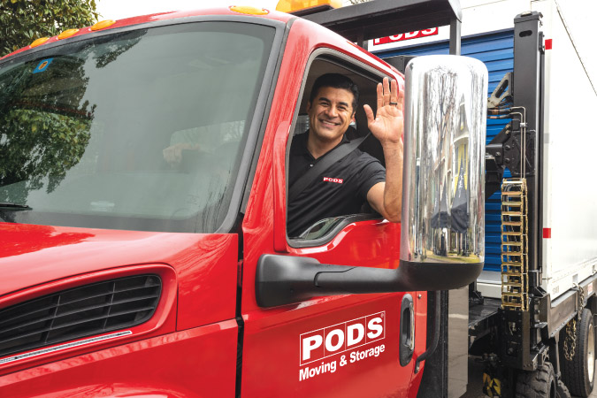 A friendly PODS truck driver is waving from the cab of his truck as he prepares to drop off a PODS portable moving container.