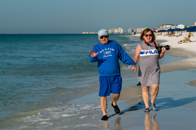 A mature couple walks hand and hand down the beaches of Sarasota, FL. Bay Village is one of the best retirement communities in the U.S. if you're looking for living near the water.