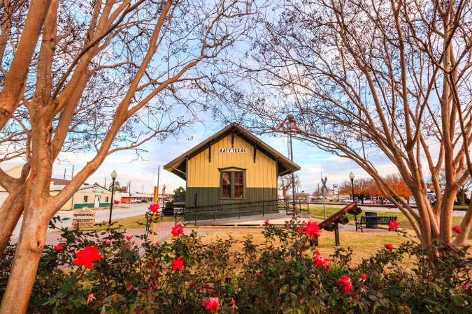 View over the top of blooming rose bushes of a train station in Katy, Texas, during the golden hour.