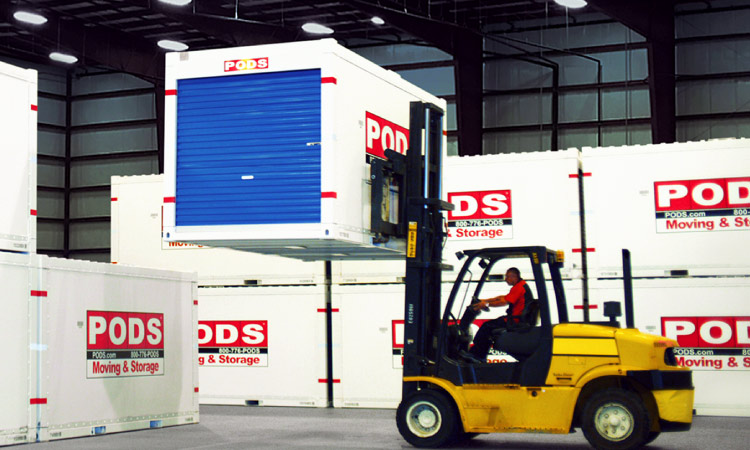 A forklift driver skillfully positions a PODS storage container for placement atop another container in a secure PODS storage facility.