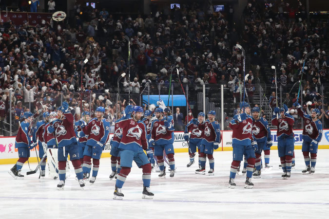 The Colorado Avalanche hockey team skates around on the ice surrounded by bleachers filled with their fans.