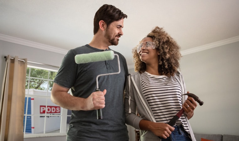 A couple holding tools for remodeling their small kitchen with a PODS storage container outside