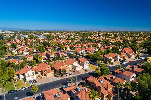 An overhead shot of the Phoenix suburbs on a bright, sunny day. Cars are parked in driveways and there are trees on every street.