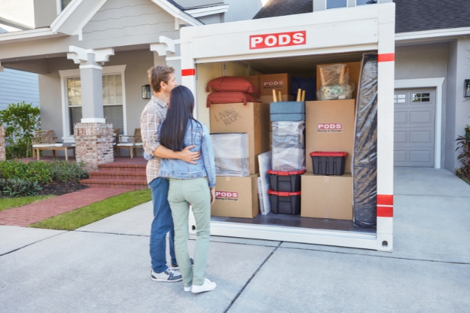 A couple living in Delray Beach stands in the driveway of their new home in front of an open PODS portable moving container filled with furniture and boxes.
