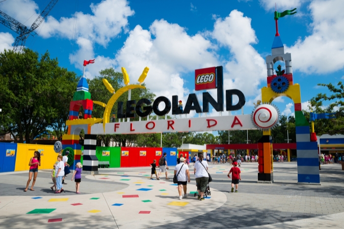 Families walking through the colorful LEGO-themed entrance at LEGOLand Florida Resort in Winter Haven, Florida, on a partly cloudy day.