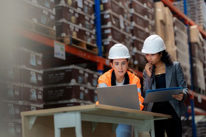 Facilities staff reviewing inventory and safety information in a warehouse as part of facilities management.
