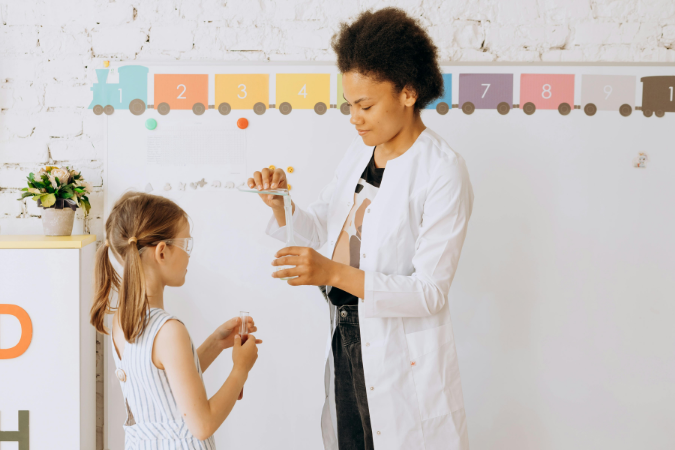 A young teacher stands in her classroom with a student, conducting a science expirament.