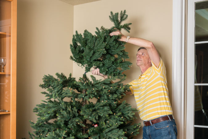 A senior man is removing the top of his artificial Christmas tree while preparing to put it away in Christmas tree storage until next year.