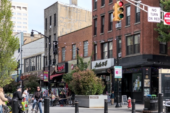 A bustling Historic Downtown — one of the best neighborhoods in Jersey City — with pedestrians strolling past shops and restaurants along the Pedestrian Plaza.