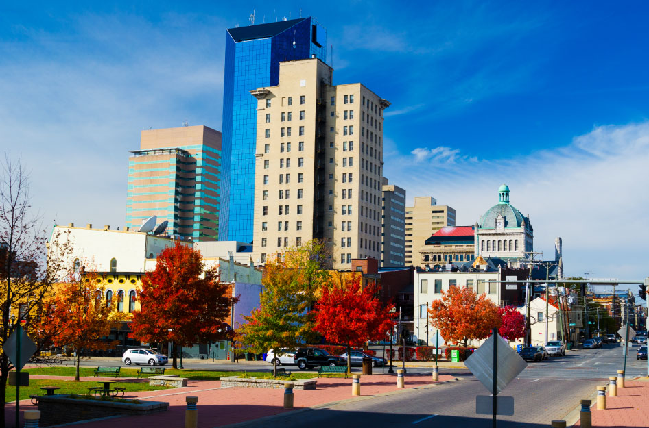 View of the Downtown Lexington skyline on a sunny day, featuring distinct city buildings, vibrant red foliage, and a bright blue sky.