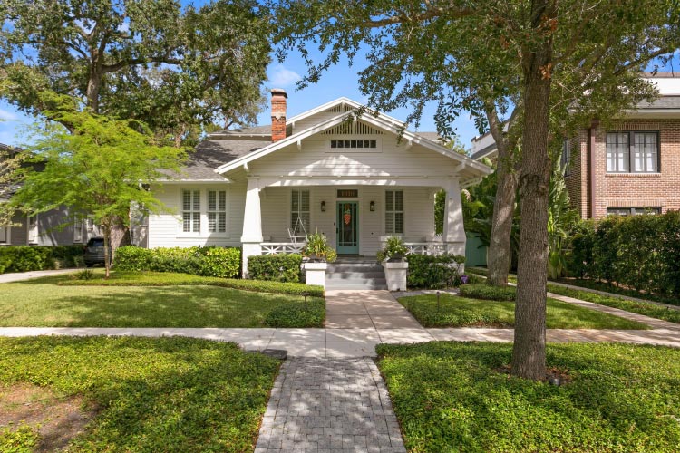  A lovely white bungalow in Tampa’s Historic Hyde Park neighborhood. The home features a wide covered porch, a chimney, and a shaded lawn.