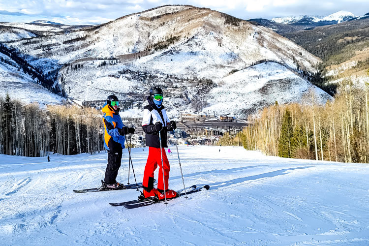 A retired couple dressed in full ski gear is posing for a photo on Vail Mountain in Vail, one of the best places to retire in Colorado. 