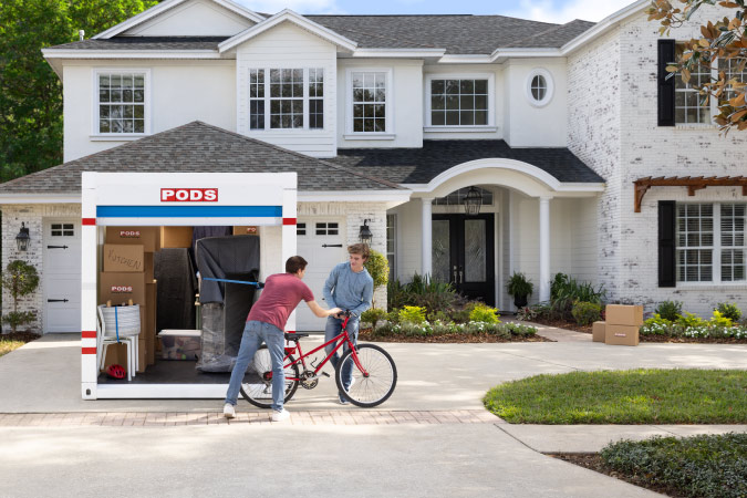 A man is unloading a bicycle from a PODS container and handing it to his teenage son after moving to one of the places that pay you to live there.