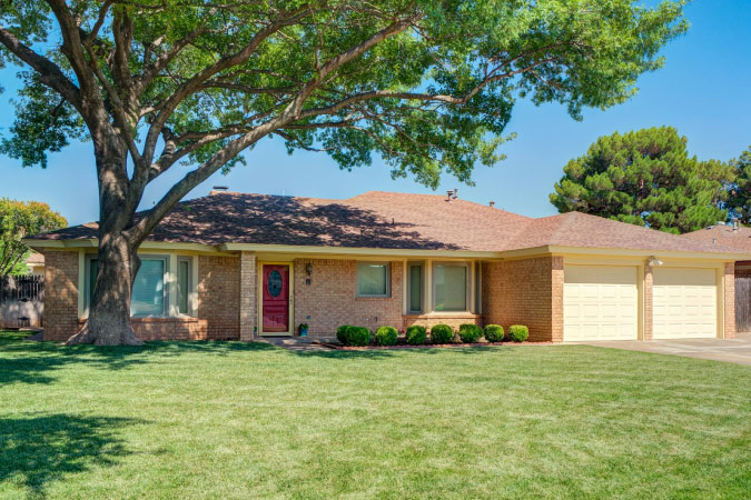 A lovely, one-story home is shaded by a mature tree in Raintree — one of the best Lubbock neighborhoods