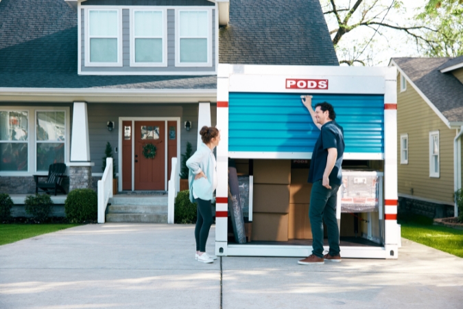 A pregnant woman and her husband are standing in their driveway beside a PODS portable moving container, ready to unload their belongings and start officially living in Ocala, FL.