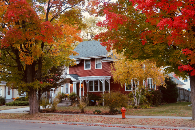 A red home, partially hidden by fall trees in Rochester, NY.
