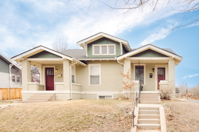 Street view of a duplex in Denver’s Regis neighborhood, featuring an elevated lawn with twin covered entrances on either end of the building.
