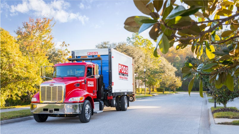 A truck carrying a PODS container is driving down a residential road in one of the best small towns in Florida.